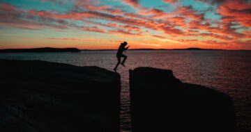 man leaping over cliff sunset
