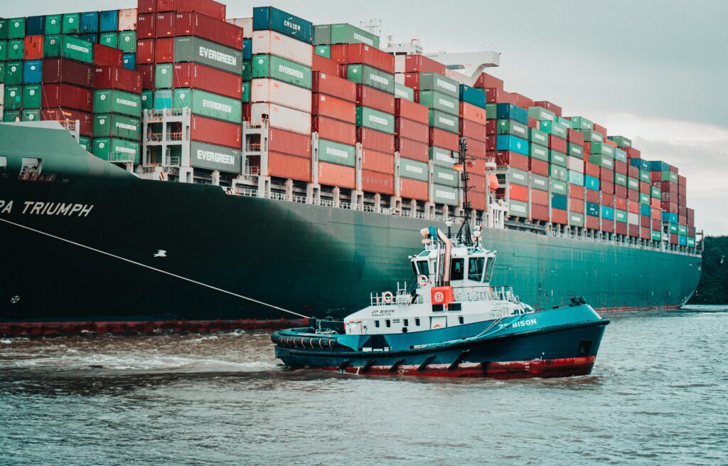 Tug towing large cargo vessel with lots of containers. Photo by Mika Baumeister on Unsplash.
