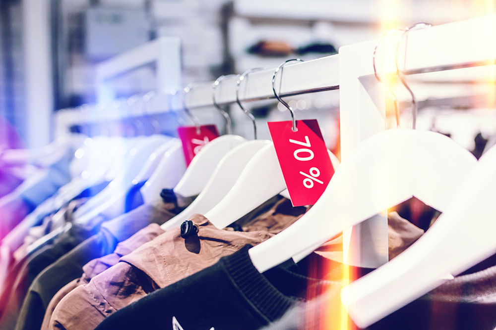 Garments hanging in a clothing store. Some garments have red markdown labels. Photo by Photo by Artem Beliaikin, https://unsplash.com/