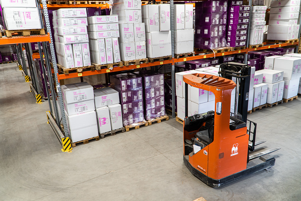 Forklift in a large warehouse with products stacked on large metal shelves. Photo by Petrebels on Unsplash